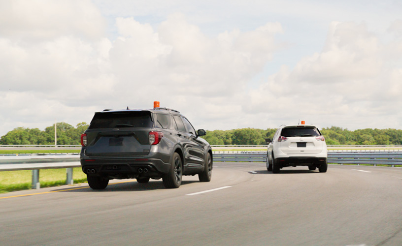 Image of a gray and white car driving in close proximity to each other around a bend of curvature on the road.