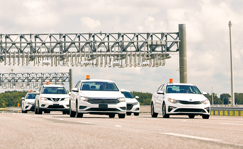 Image of five white vehicles driving under one of the four toll gantries