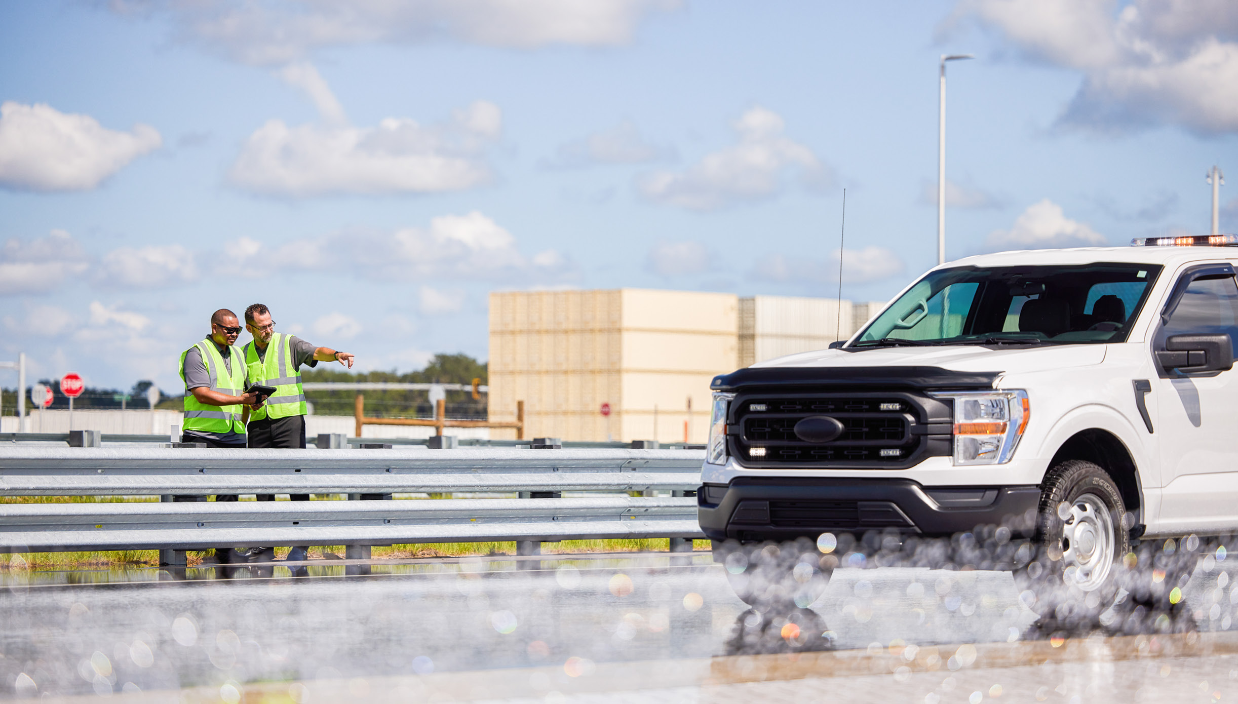 Two engineers overseeing the testing of a white truck as it drives through the water on the Wet Test Track