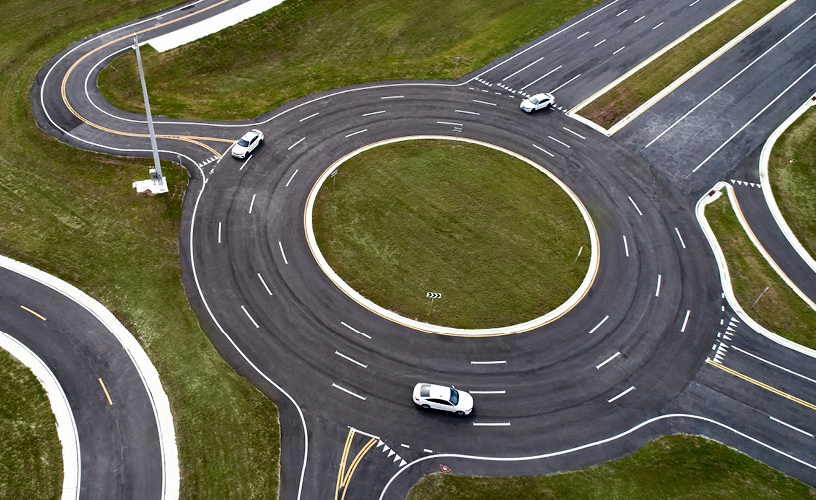 Overhead view of a roundabout with three white cars driving