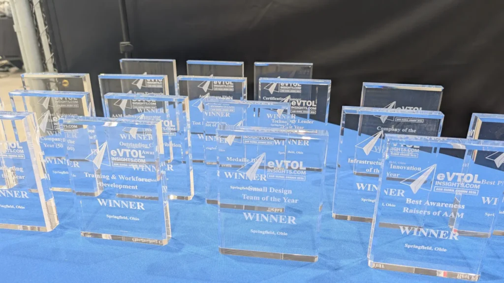 A row of blue glass awards labeled WINNER on a blue table at an awards ceremony display area.