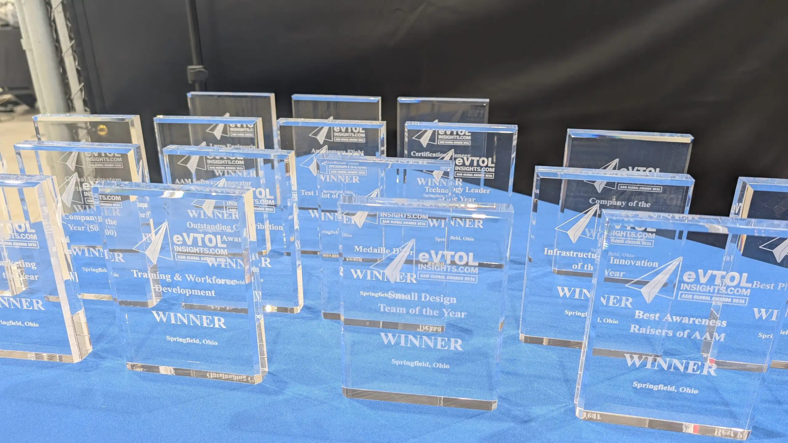 A row of blue glass awards labeled WINNER on a blue table at an awards ceremony display area.