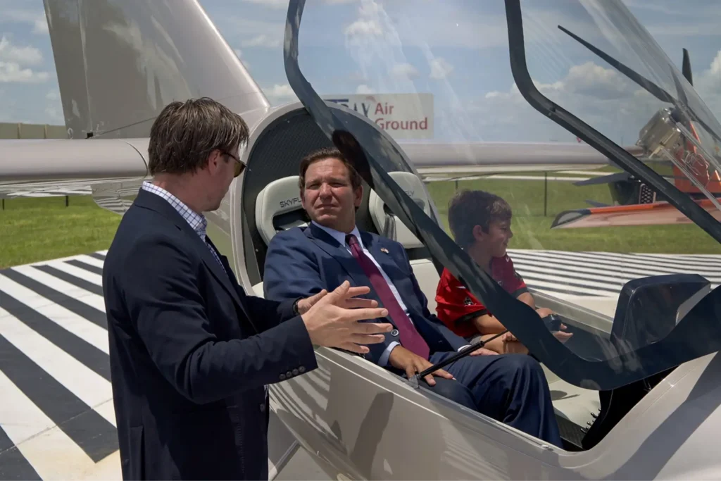 Florida Governor Ron DeSantis speaks with an eVTOL representative as he sits in an eVTOL with his Son.